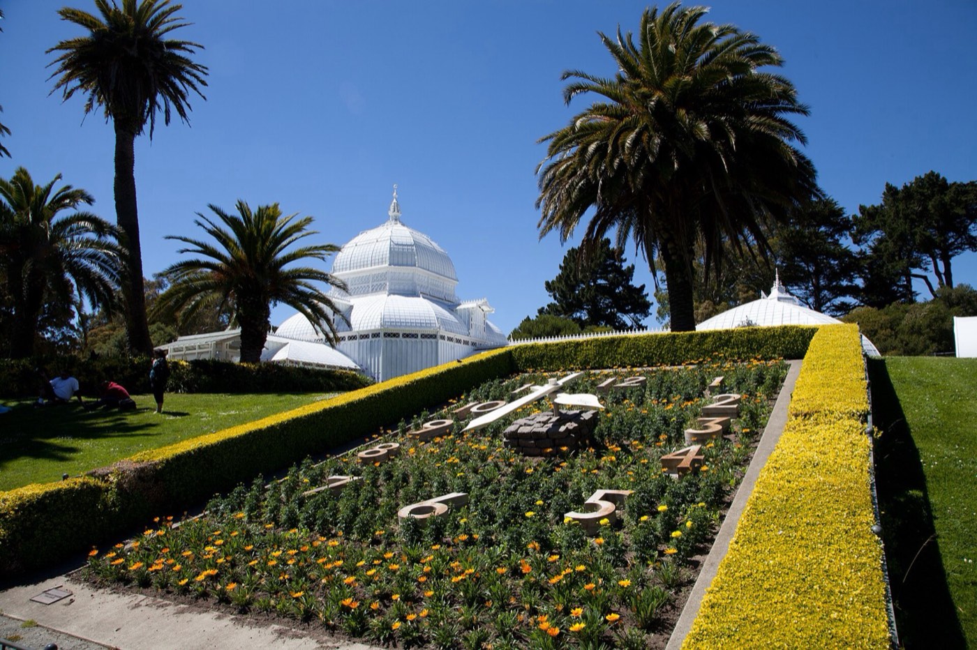 The white glass domes of the Conservatory of Flowers behind palm trees and a flower bed