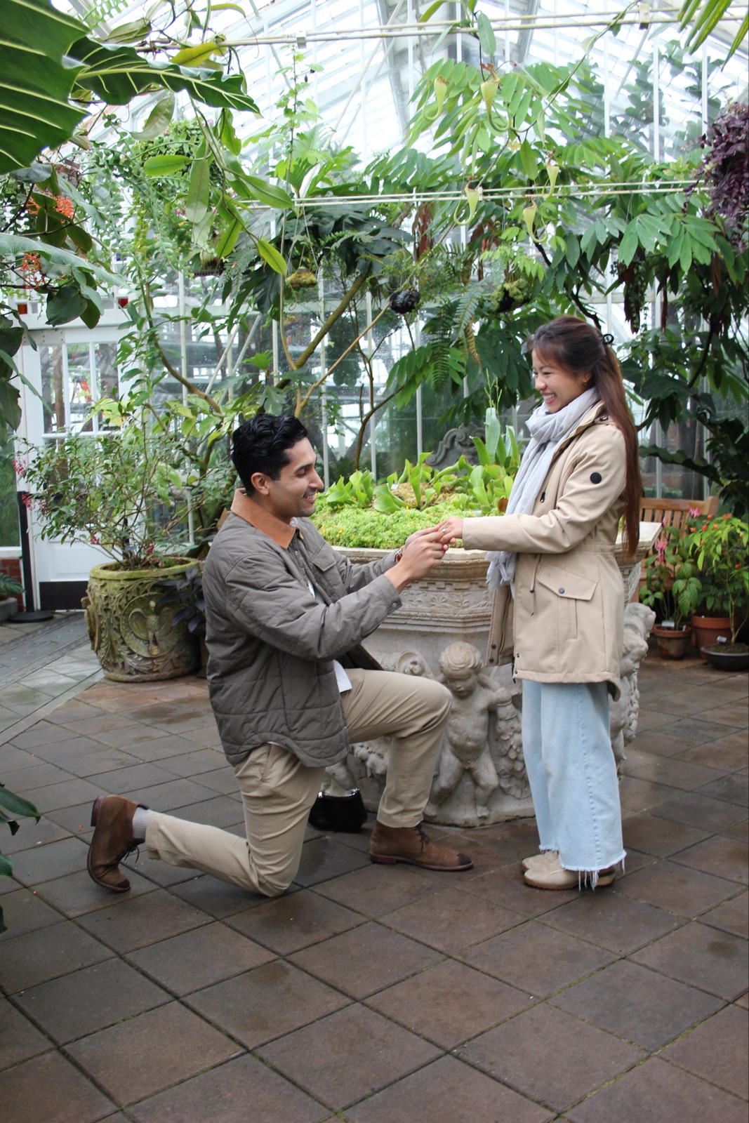 Juan Pablo kneeling and holding Trinique’s hand among the conservatory plants
